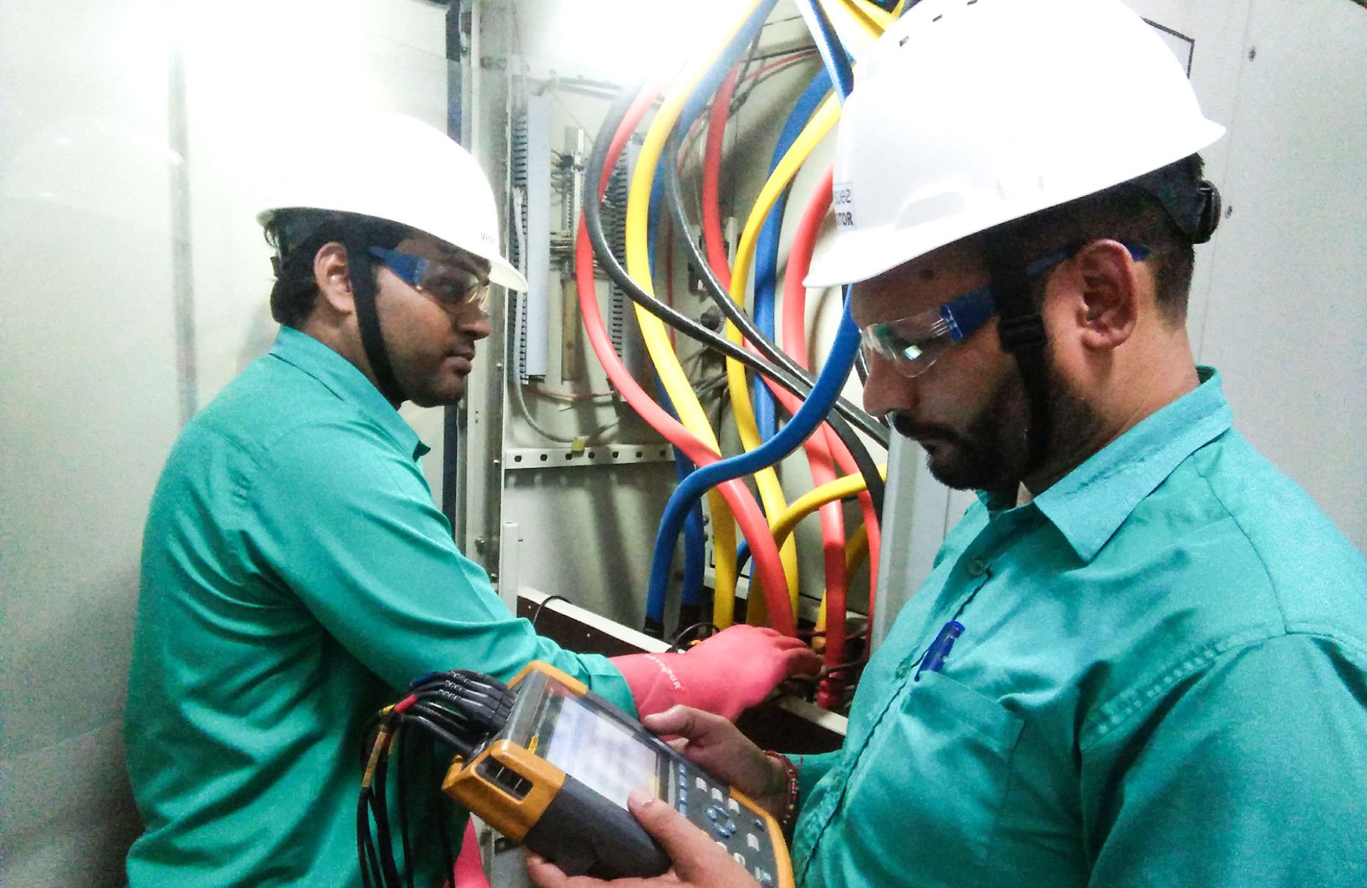 Power quality audit technicians checking electrical panel with analyzer for voltage fluctuations and power performance